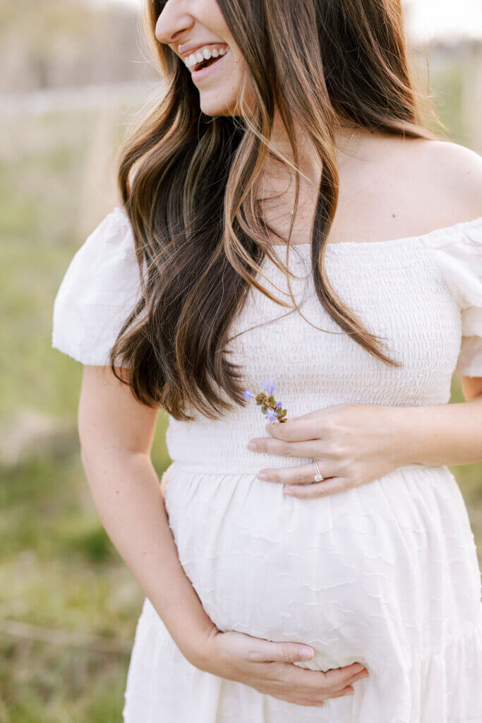 At a maternity session in Doylestown, Pennsylvania, a pregnant mother holds a purple flower by her belly.