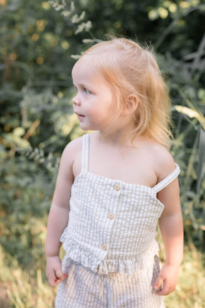 A little girl looks off in the distance, wearing a striped jumper in a family session in Doylestown, Pennsylvania.