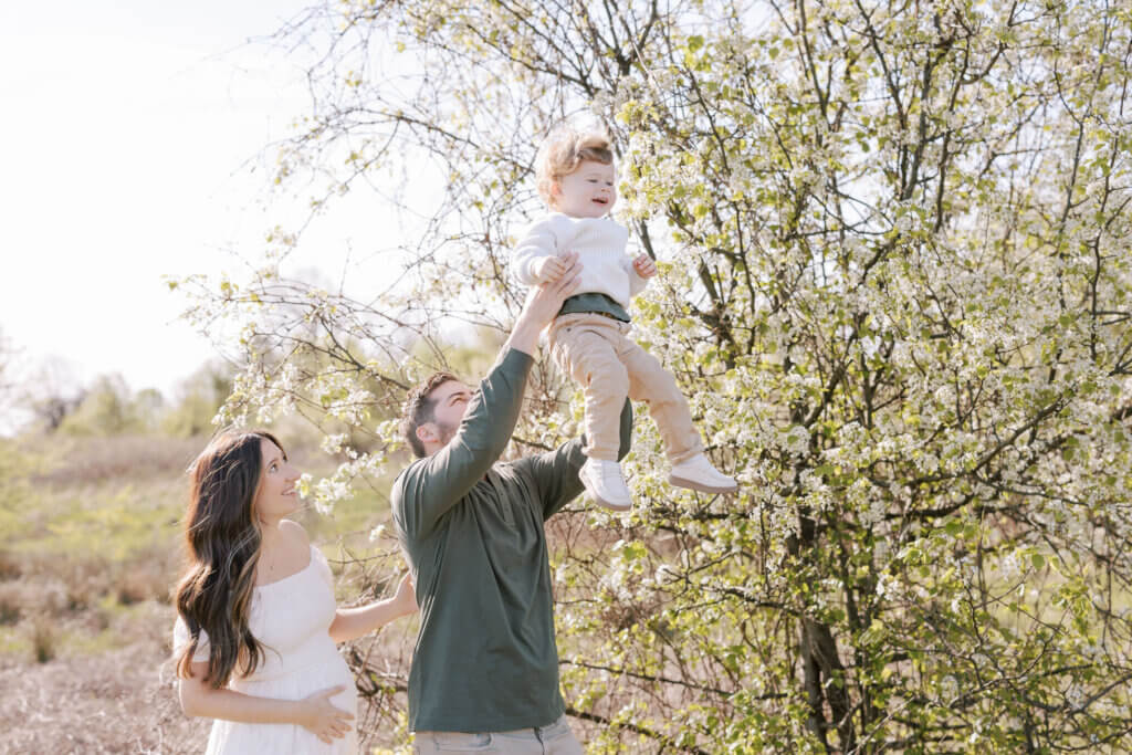 At a maternity session in Doylestown, Pennsylvania, a mom and dad lift their baby boy amidst greenery.