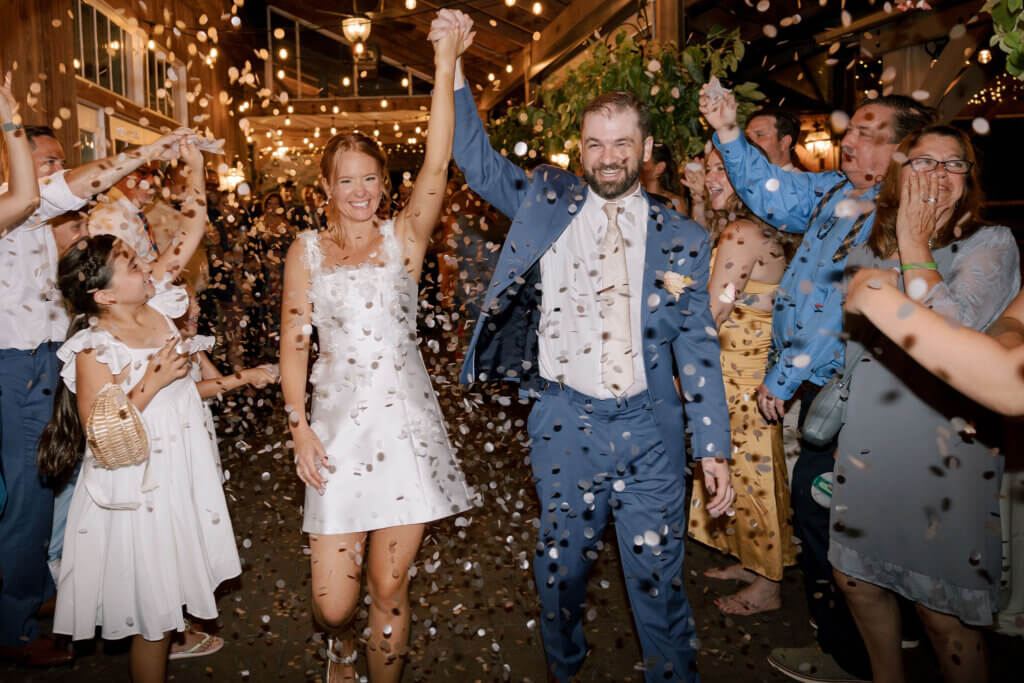 The newlywed couple raise their hands as they exit their reception while confetti falls around them at Riverdale Manor in Lancaster, Pennsylvania.