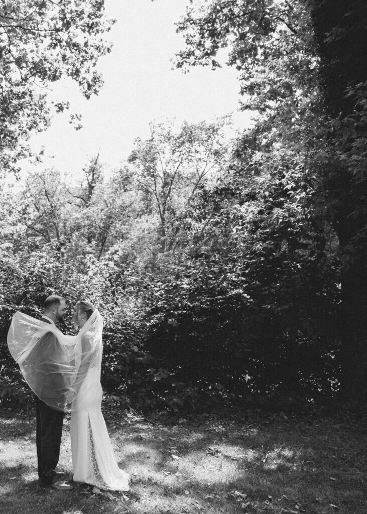 The bride and groom share a quiet moment in black and white, while her veil billows around his shoulders at Riverdale Manor in Lancaster, Pennsylvania.