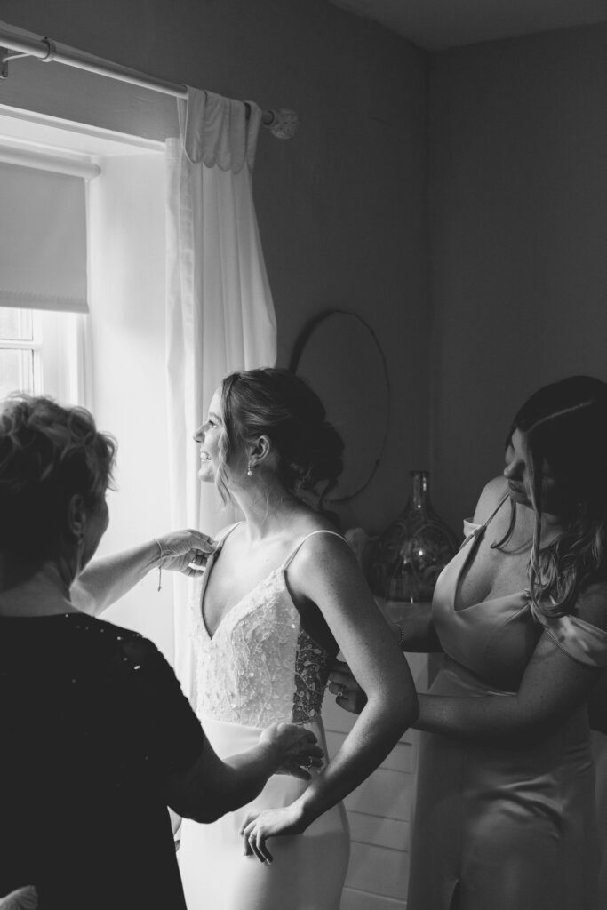 The bride's mom helps her get dressed in a black and white candid shot at Riverdale Manor in Lancaster, Pennsylvania.