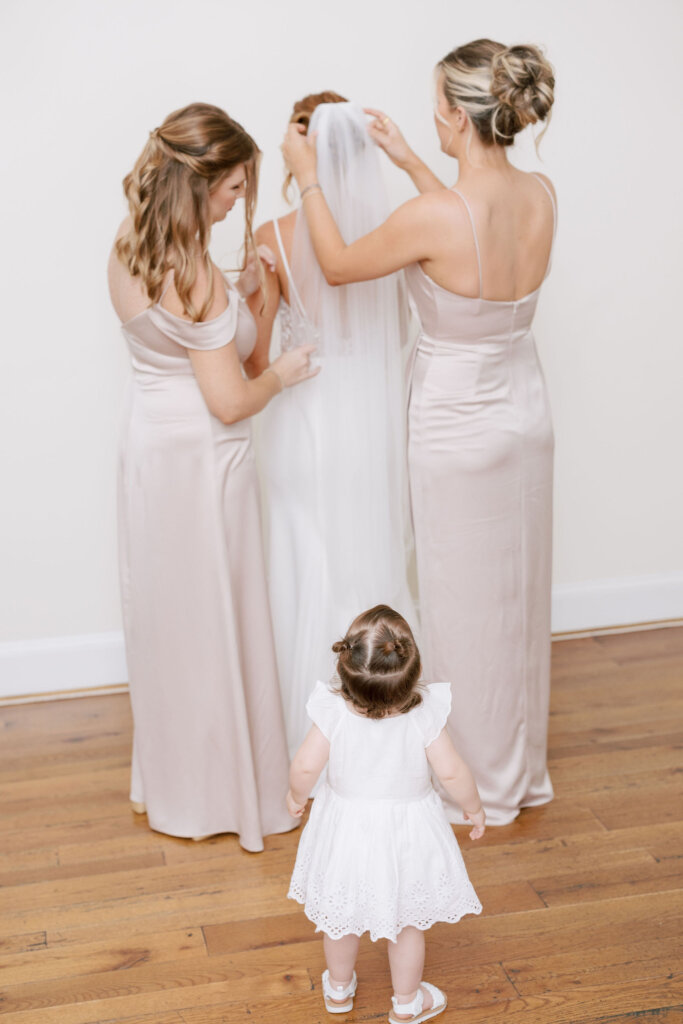 A toddler looks on as two bridesmaids help secure the bride's veil prior to her wedding ceremony at Riverdale Manor in Lancaster, Pennsylvania.