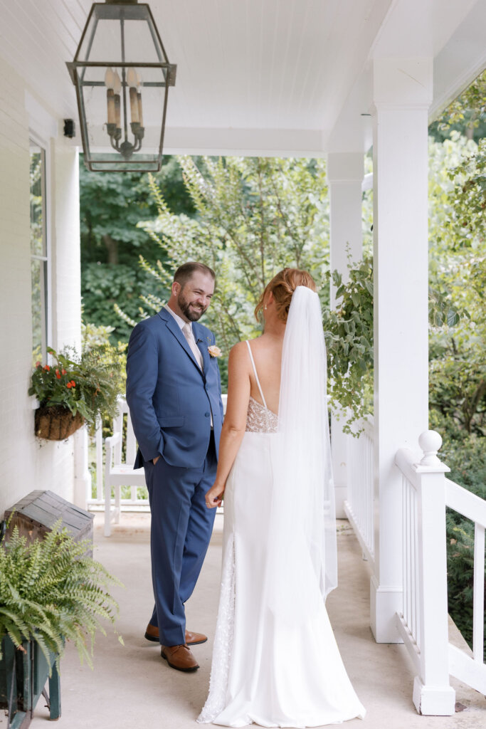 A bride and groom smiling at each other on the wrap-around porch of Riverdale Manor in Lancaster, Pennsylvania.