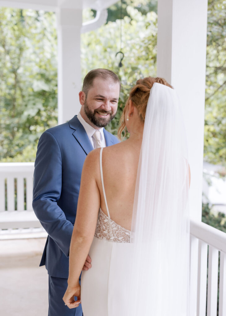 A bride and groom smiling at each other on the wrap-around porch of Riverdale Manor in Lancaster, Pennsylvania.