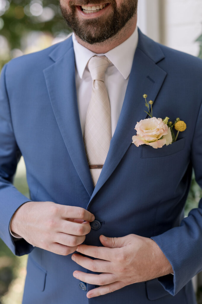 A close-up of the groom's suit jacket with florals, a monogramed tie clip, and champagne tie at Riverdale Manor in Lancaster, Pennsylvania.