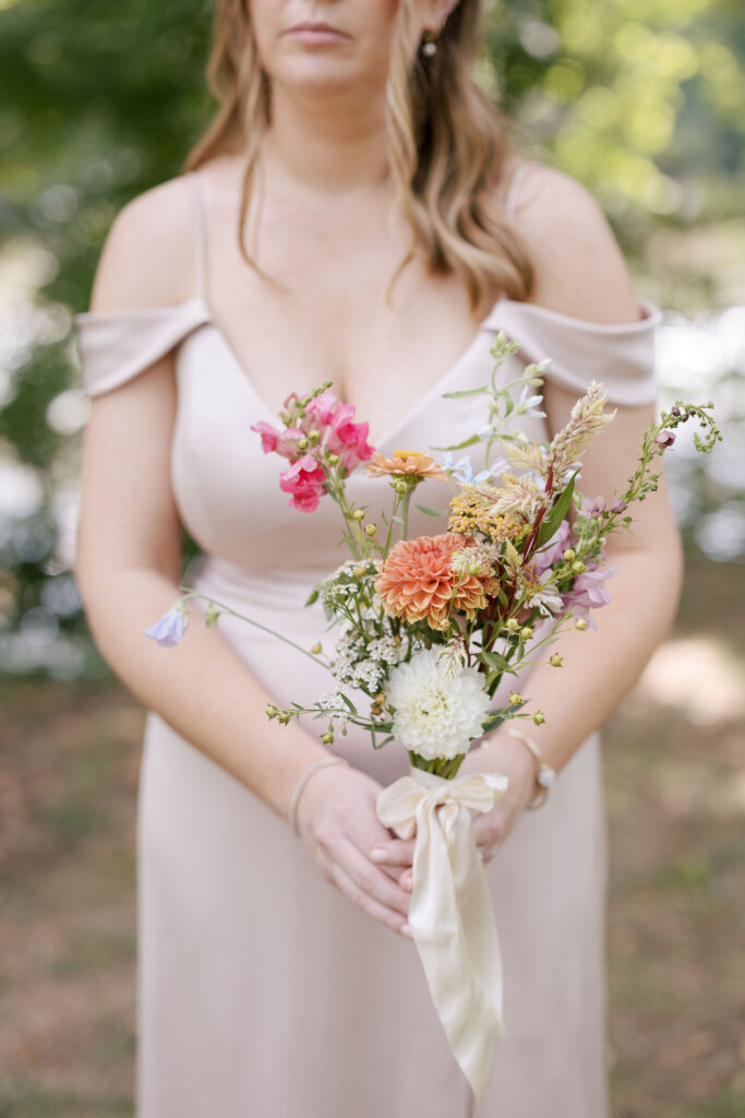 A close-up of a bridesmaid holding her bouquet, wrapped in an ivory, satin bow at a Riverdale Manor wedding in Lancaster, Pennsylvania.