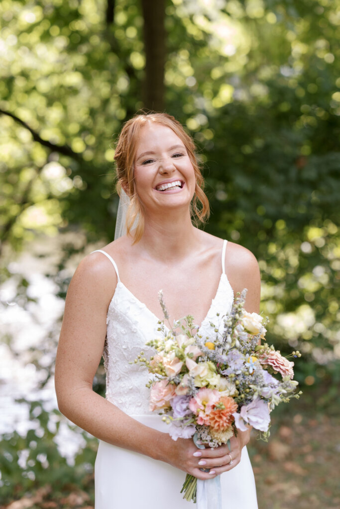 A bride smiles brightly, holding her bouquet from Waverly Flower Co. at Riverdale Manor in Lancaster, Pennsylvania.