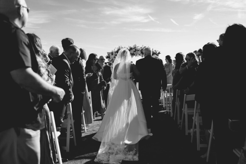 The bride is escorted by her father down the aisle of her ceremony at the Rehoboth Beach Country Club. 